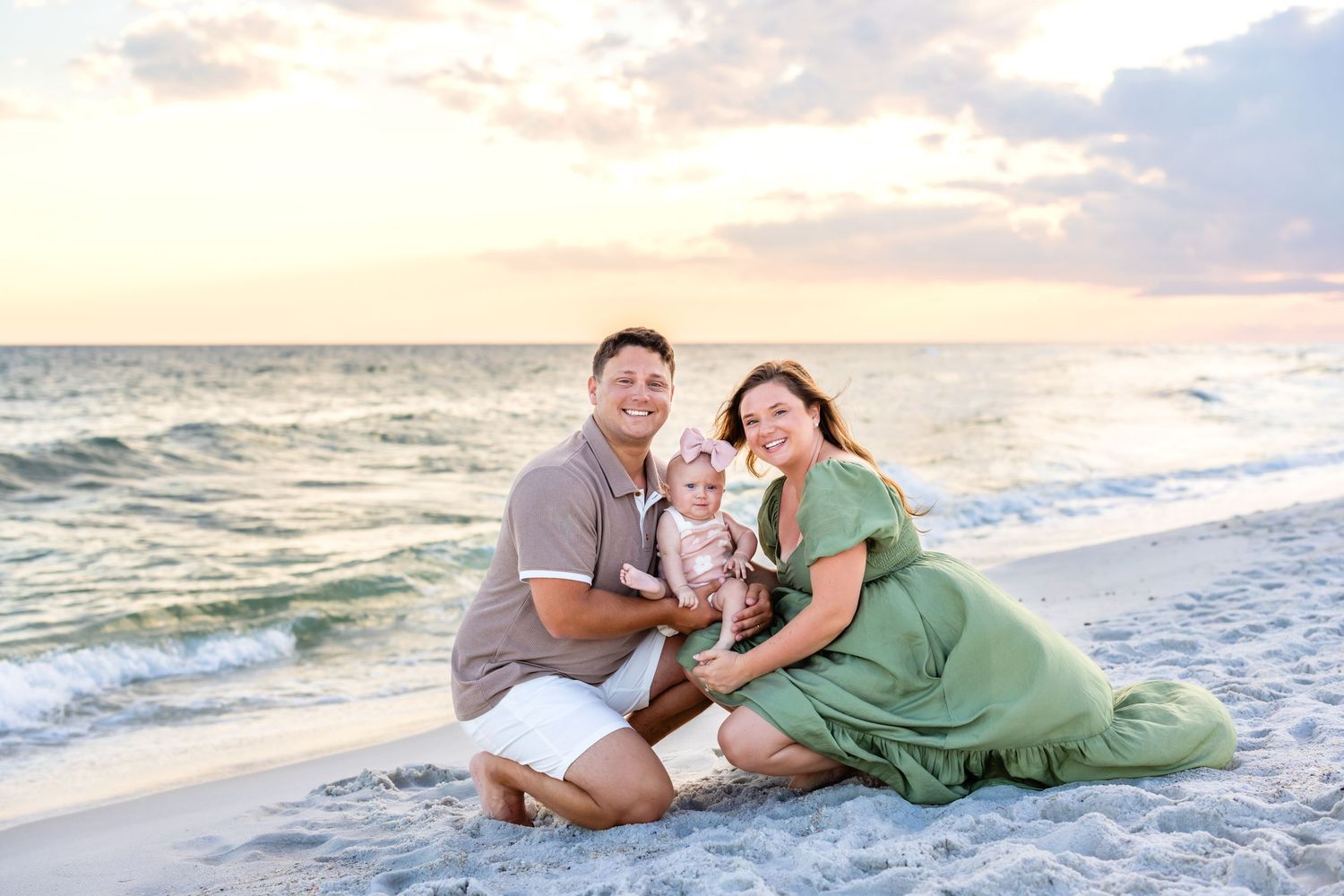 A couple poses for romantic sunset photos along a sandy beach with gentle waves in the background.