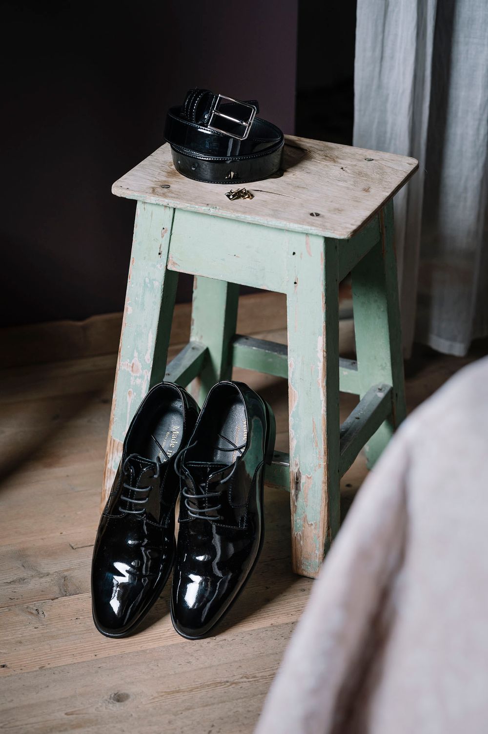 Black patent leather dress shoes and belt arranged on mint green wooden stool.