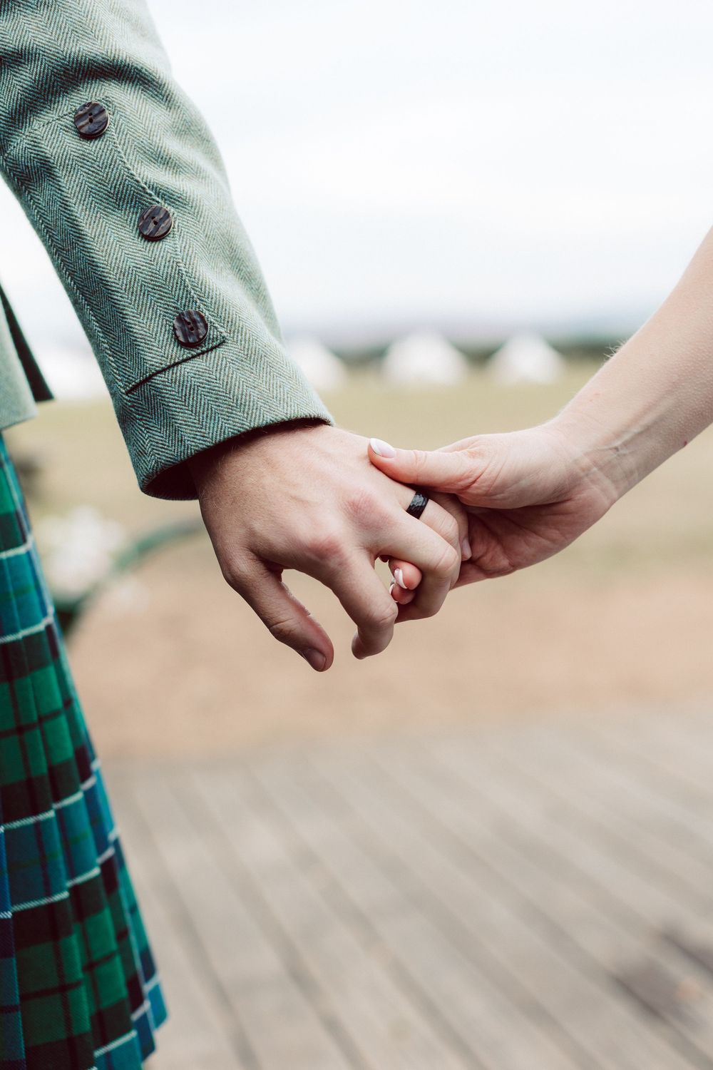 Close-up view of two hands holding each other tenderly against a blurred background with green plaid fabric details.