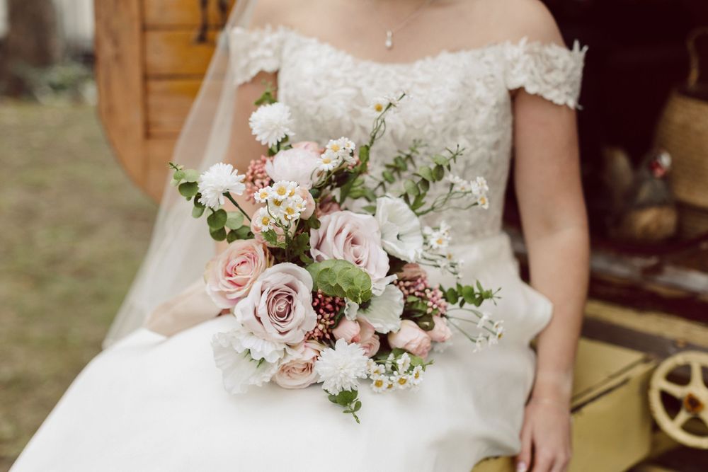 A wedding bouquet featuring soft pink roses, white flowers and delicate greenery held against a white dress.