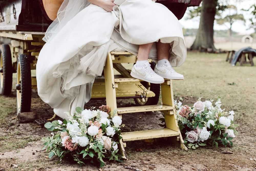 Close-up shots of white wedding shoes with delicate floral arrangements on a rustic wooden bench.