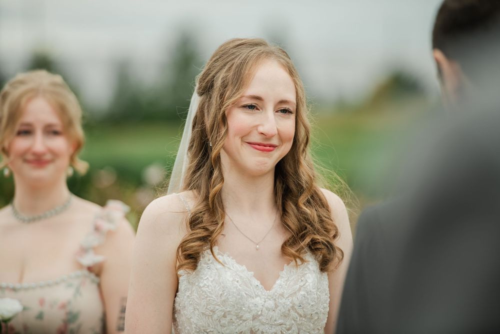 A row of bridesmaids in matching blush pink dresses stand together smiling at an outdoor wedding.