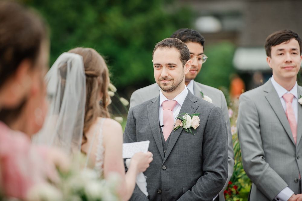 Wedding party members in gray suits and pink ties gather outdoors during a celebration.