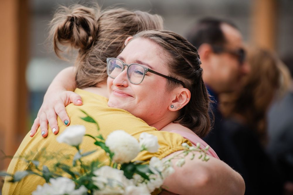 Joyful emotional embrace between people at a celebration with yellow flowers in the background.