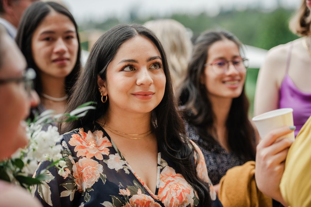 A group of wedding guests smile together in an outdoor setting wearing colorful floral and pastel attire.