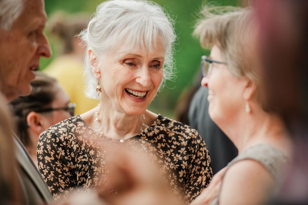 People sharing warm laughter and smiles during an outdoor gathering with natural greenery.