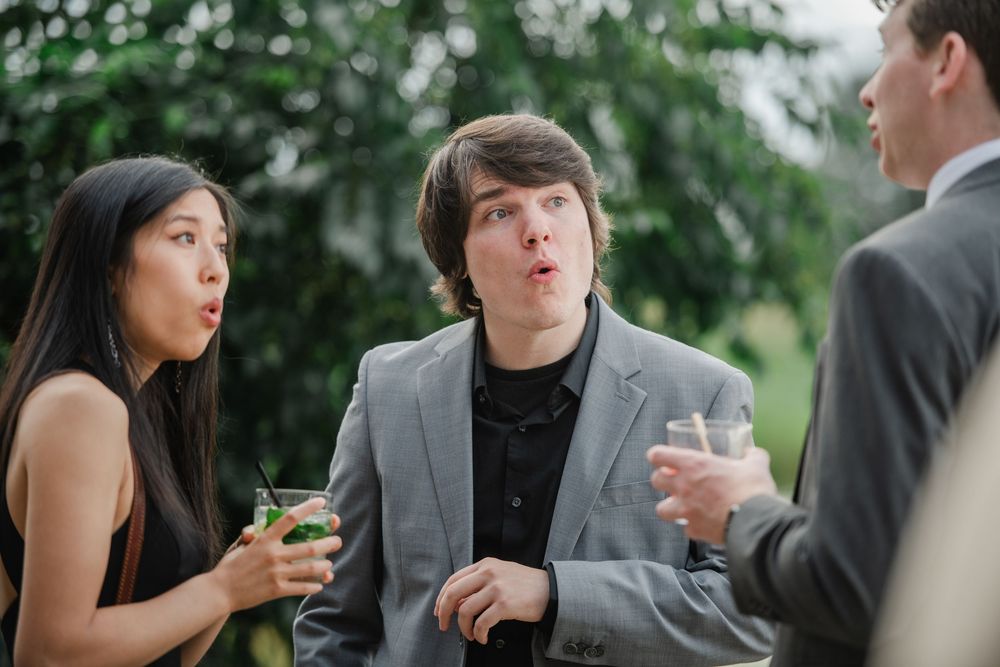 Wedding guests engage in animated conversation at an outdoor celebration.