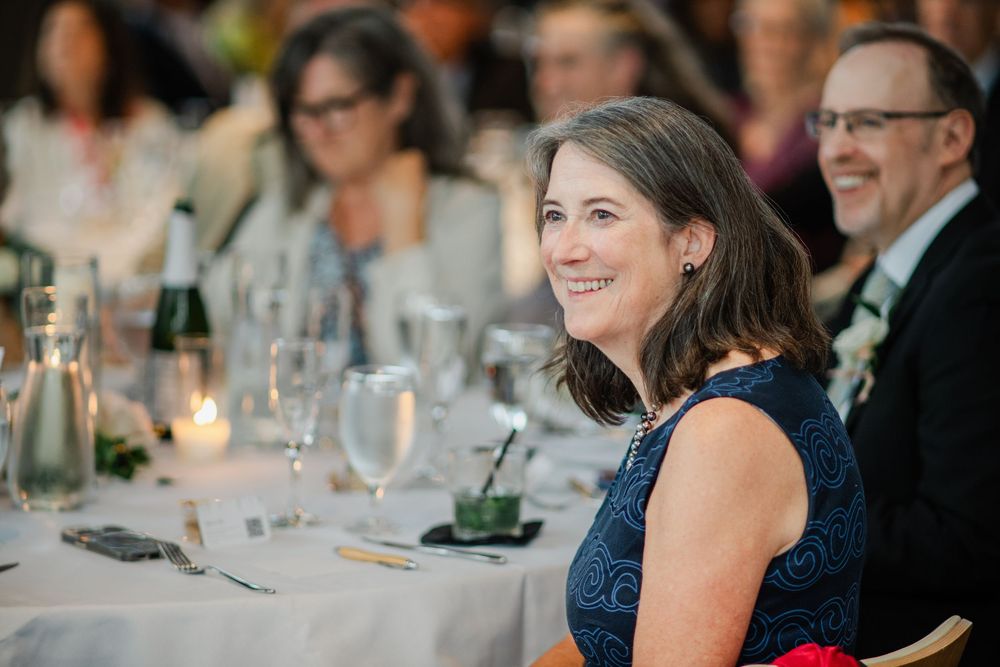 A guest in a navy blue dress smiles warmly while seated at an elegant candlelit dinner reception.