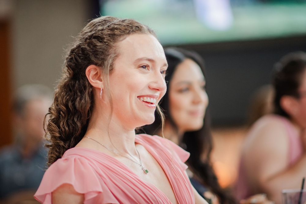 A person in a pink dress smiles joyfully while attending a social gathering.