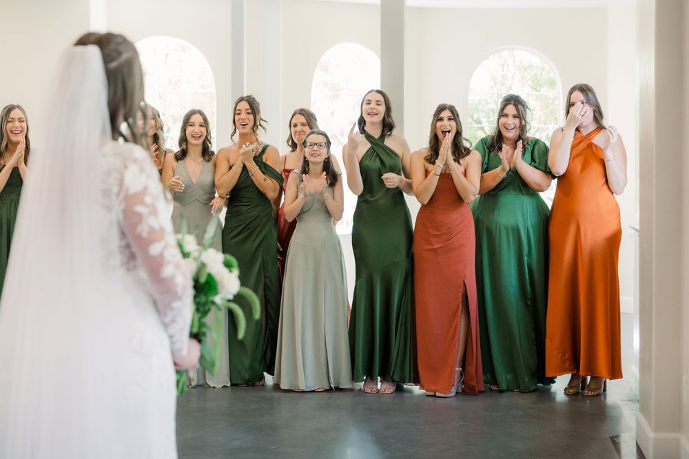 Wedding party members in coordinating green and rust orange dresses pose together in a group photo.
