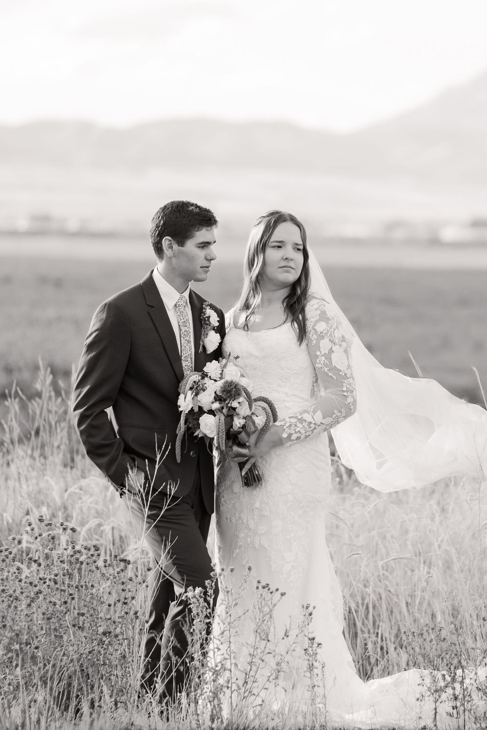 A romantic black and white wedding portrait of a couple standing together in a field of tall grass.