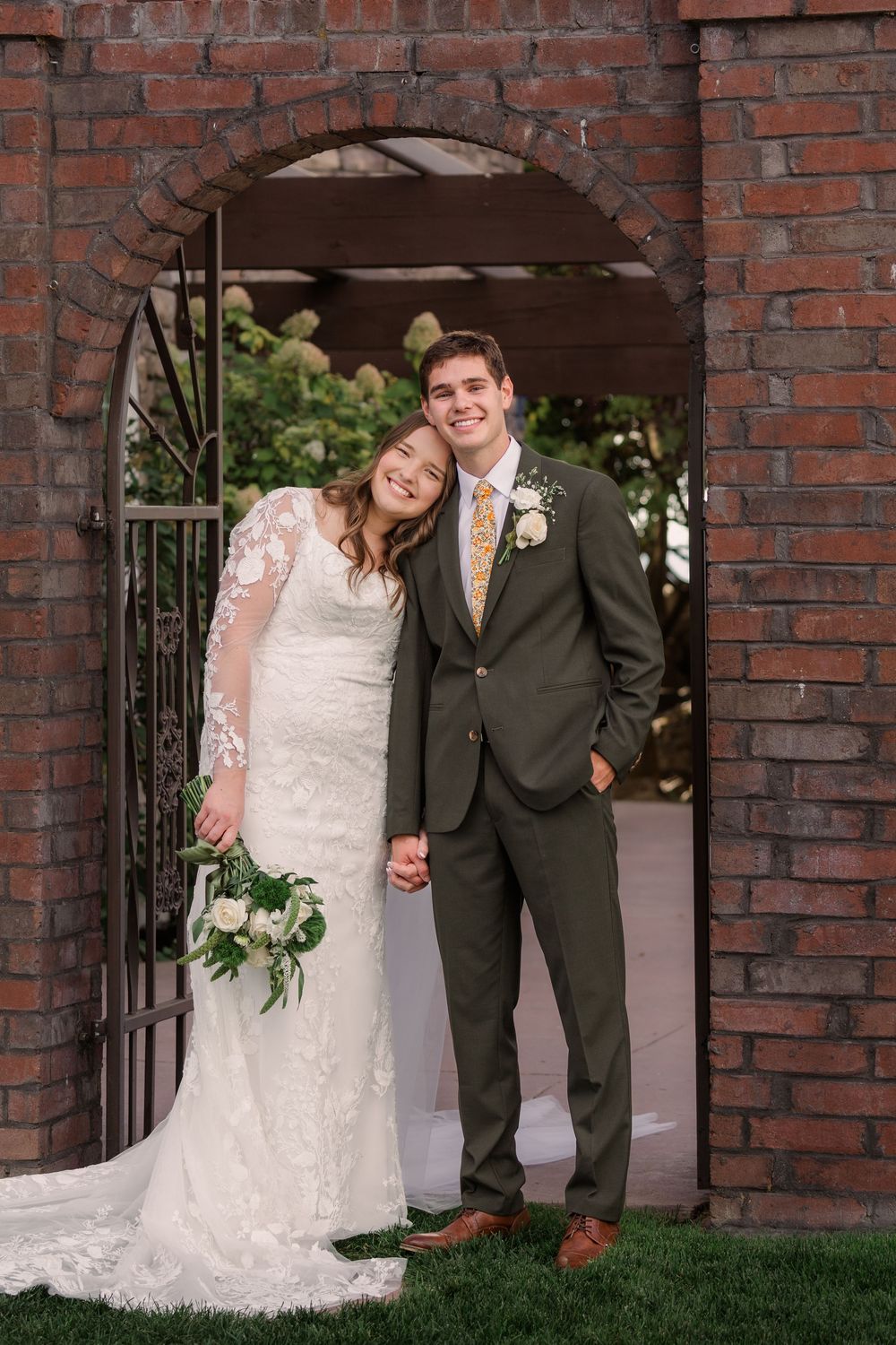 Newlywed couple poses together in front of rustic brick archway during outdoor wedding ceremony.