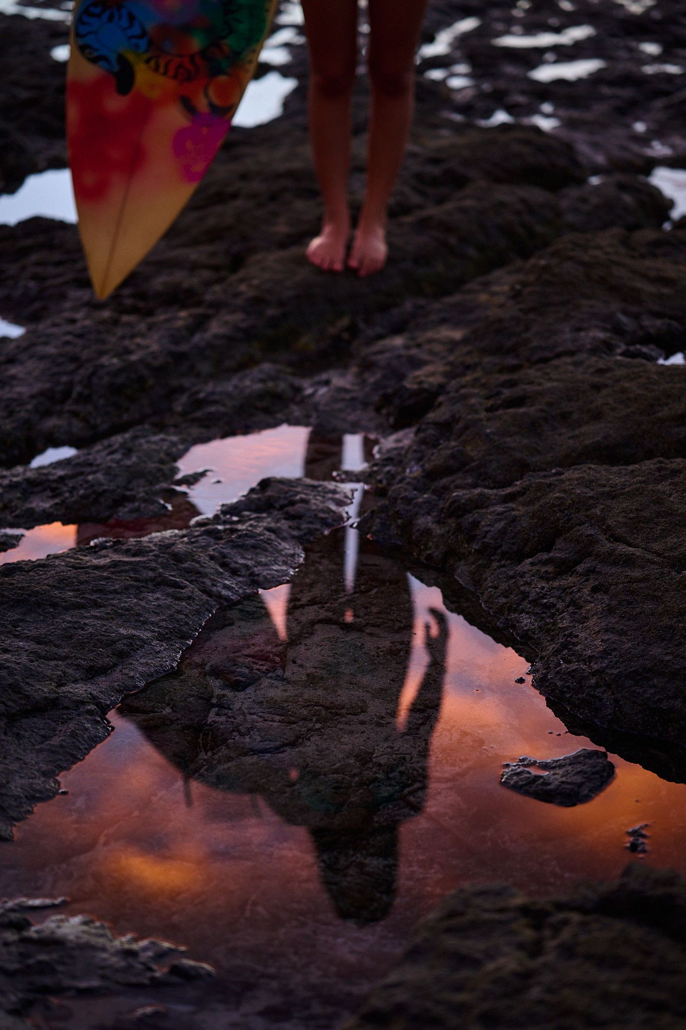 Volcanic black rocks reflect vibrant orange sunset colors in small water puddles creating a dramatic natural mirror effect.