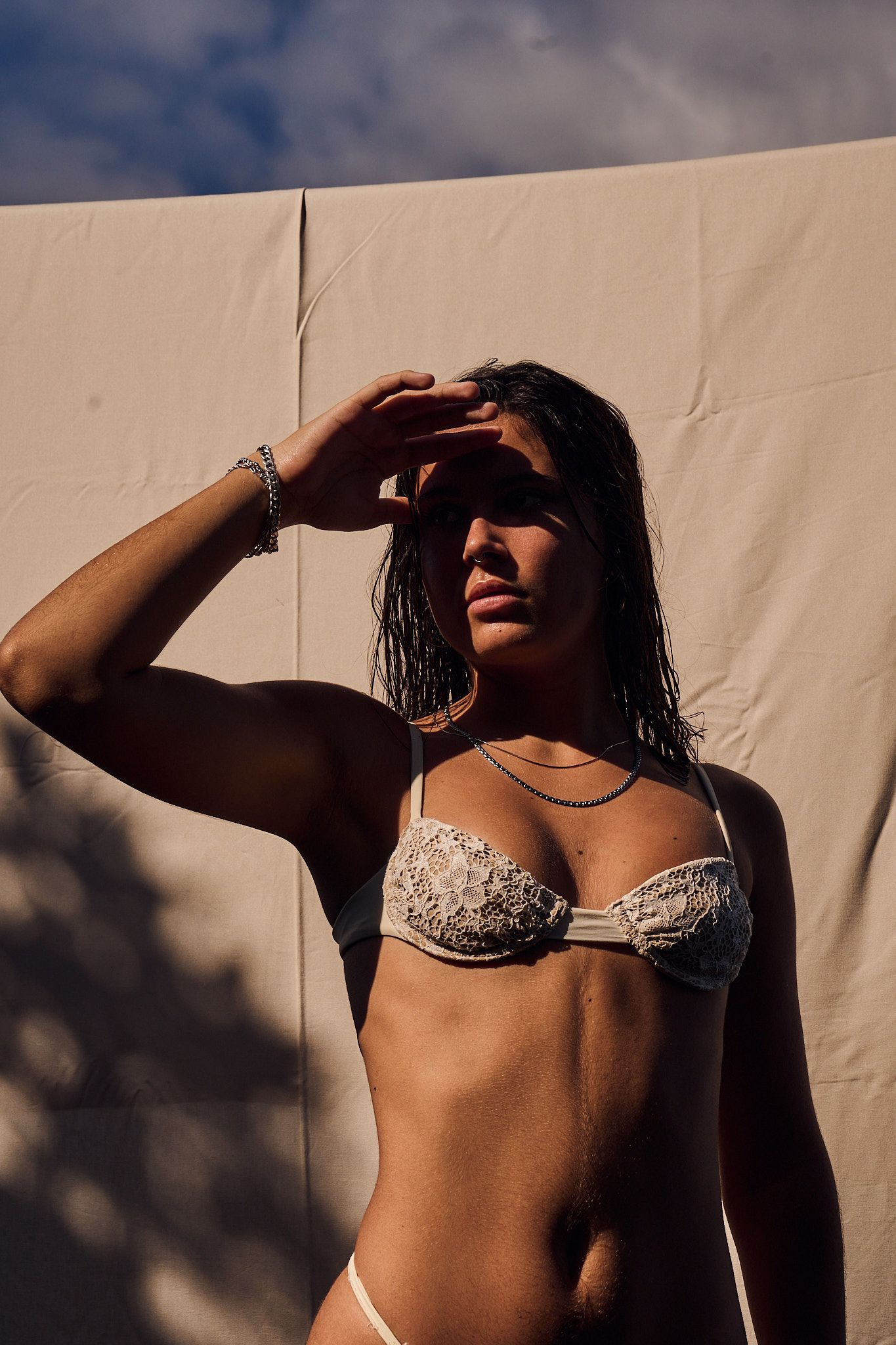 Artistic fashion photography series showing a person in a bikini top against a beige wall with dramatic shadow play.
