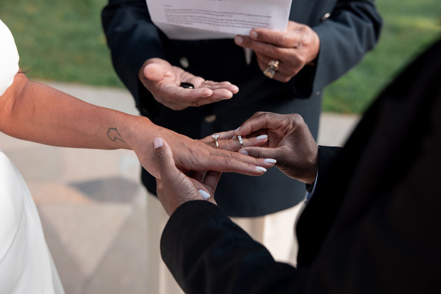 Close-up view of hands exchanging wedding rings during an outdoor ceremony.