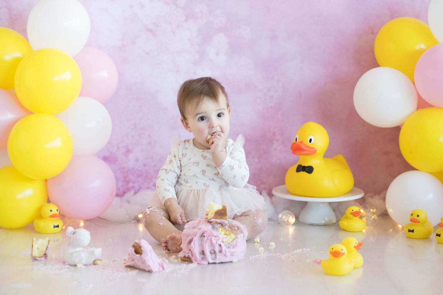 Duck-themed first birthday setup with yellow and white balloons and rubber ducky decorations.