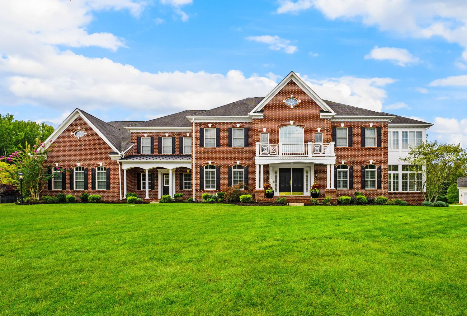 Panoramic view of a large brick mansion with manicured lawn under blue sky.
