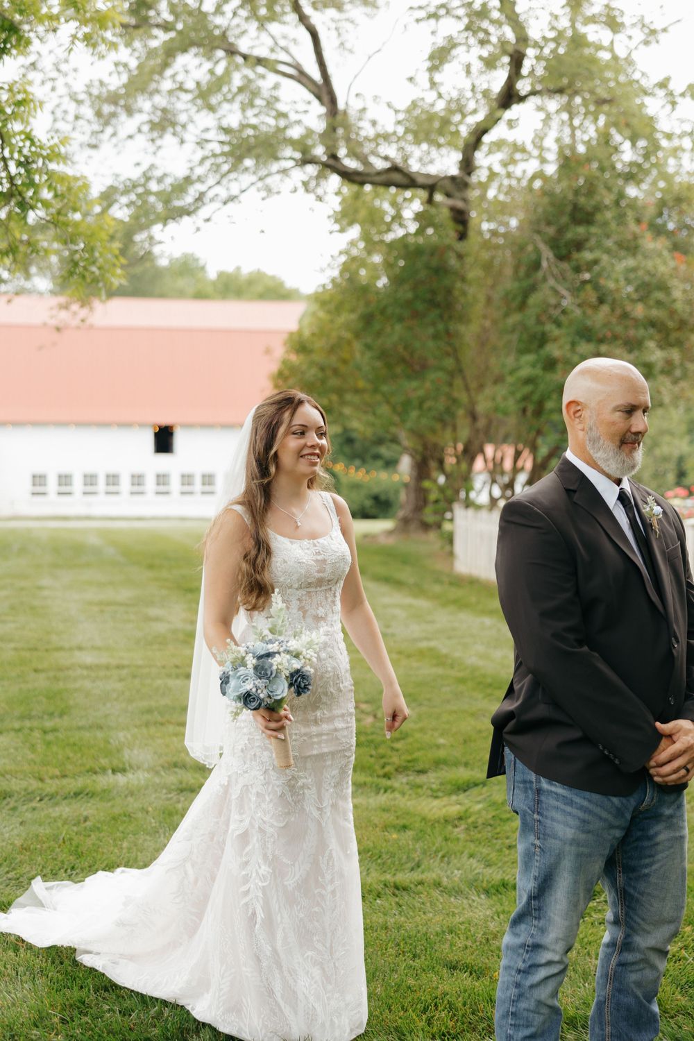 A couple walks together on a grassy lawn with trees and buildings in the background during an outdoor wedding ceremony.