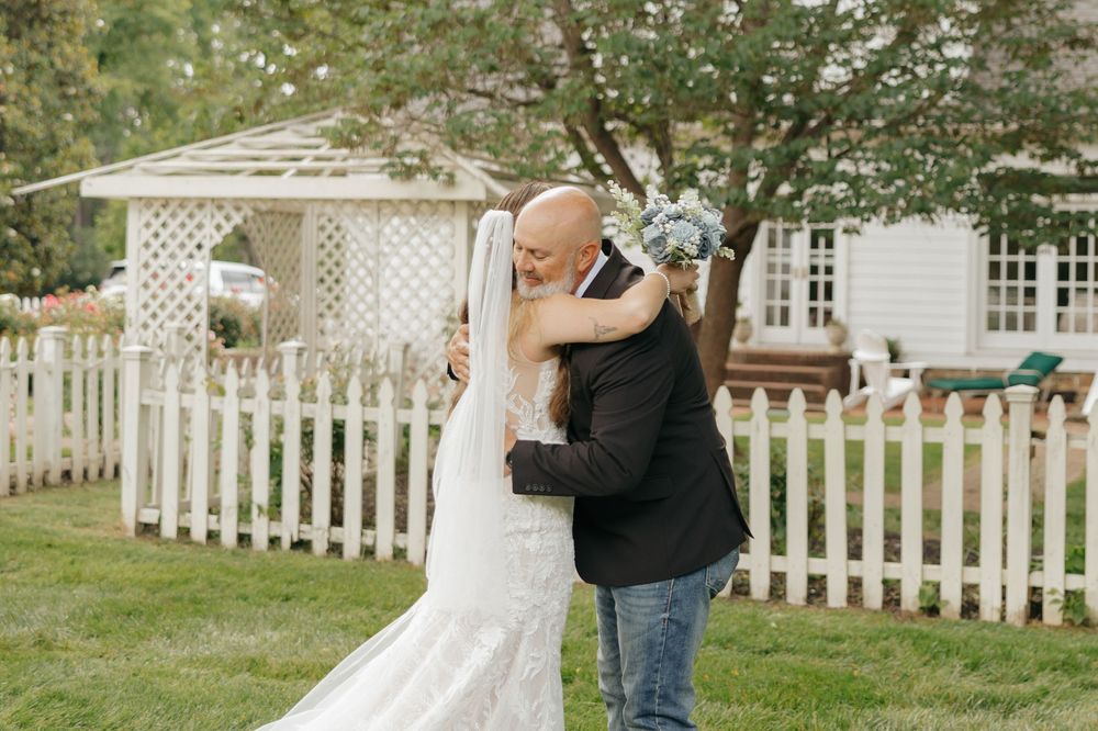 A couple embraces in a romantic moment in front of a white picket fence and garden gazebo.