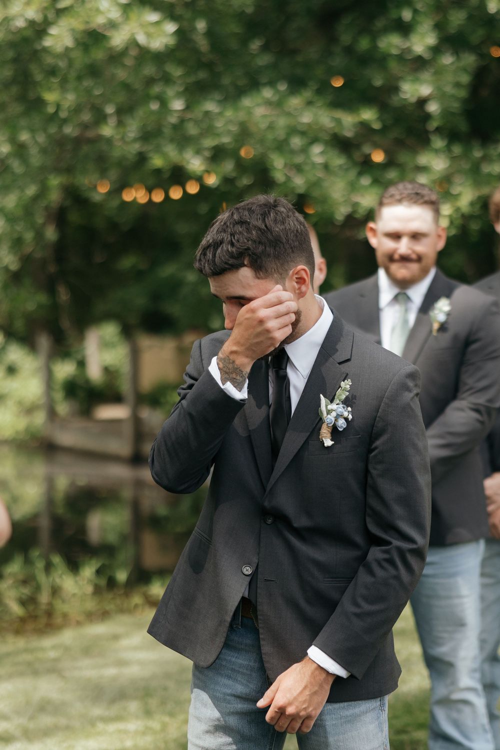 Emotional moment captured at outdoor wedding ceremony as person in black suit wipes away tears.