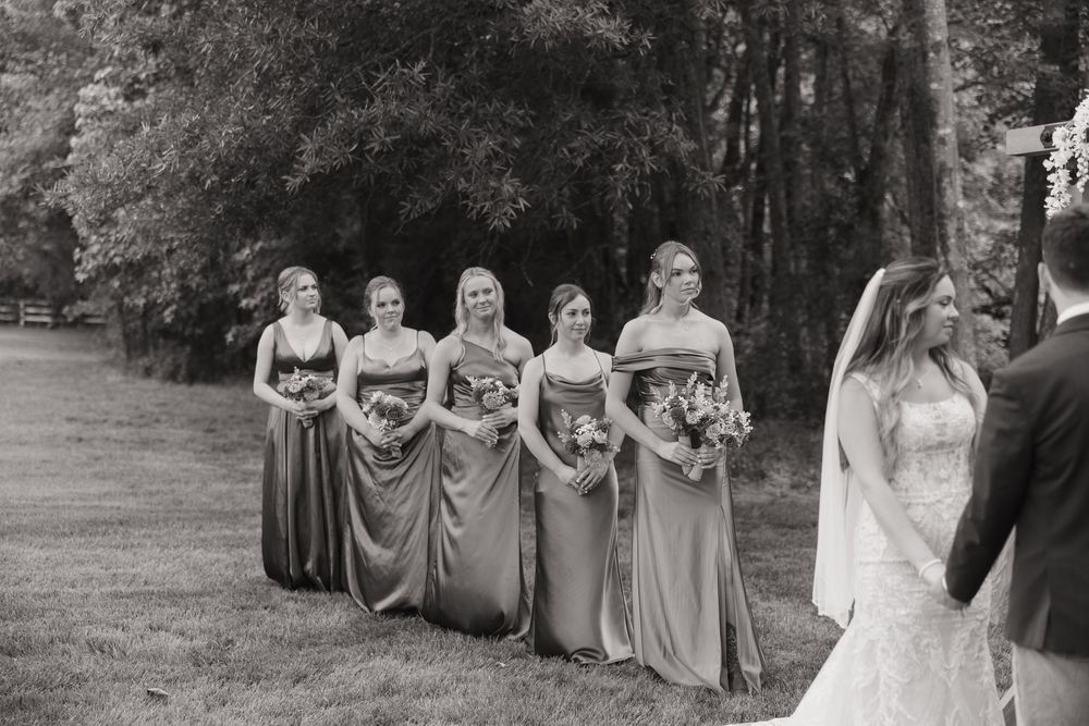 Wedding party in gray dresses and suits poses for photos in a lush outdoor garden setting.
