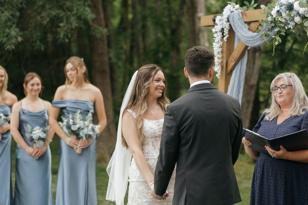 Wedding party in light blue bridesmaid dresses and dark suits pose together in an outdoor garden setting.