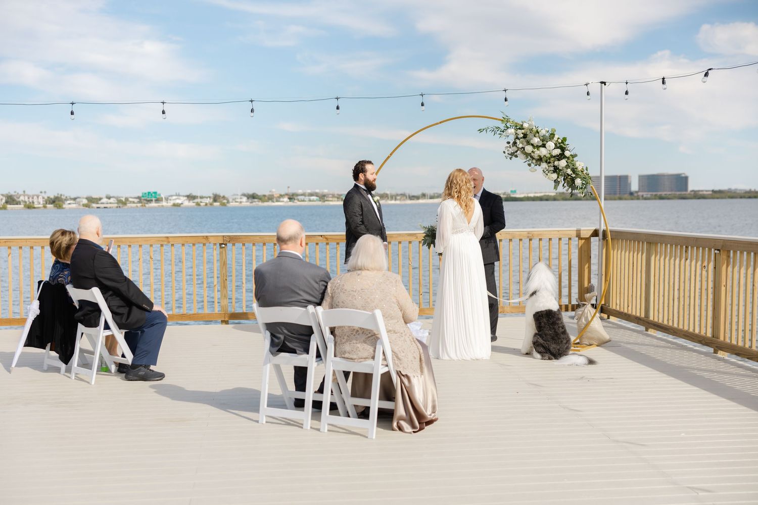 Outdoor wedding ceremony taking place on a deck overlooking the water.