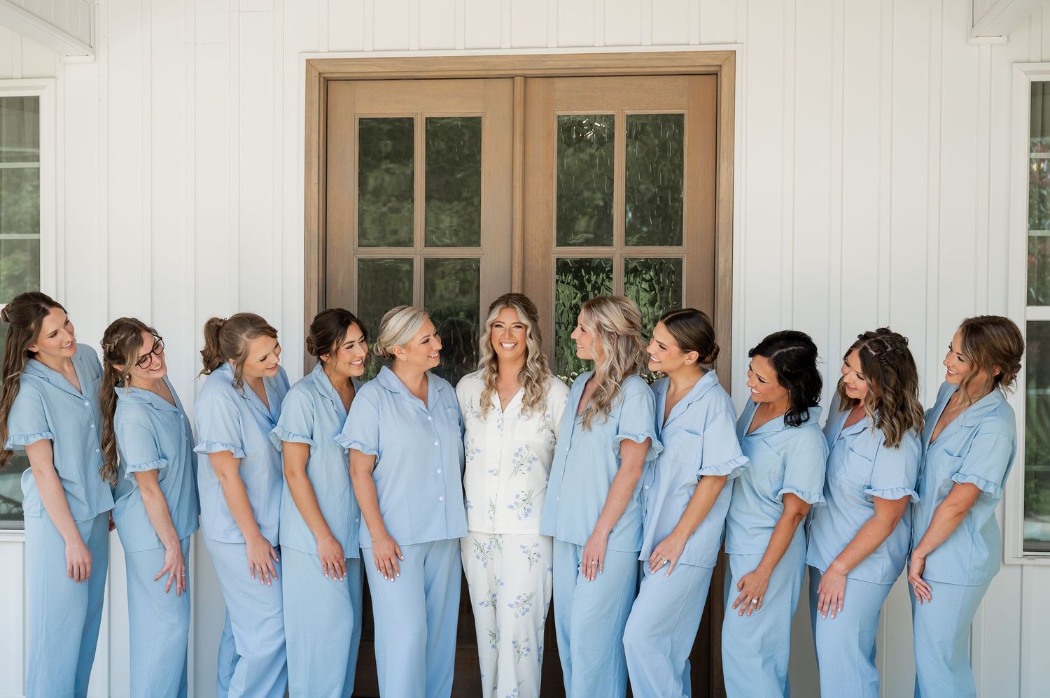 Wedding party in matching light blue dresses poses with someone in white against a white building.