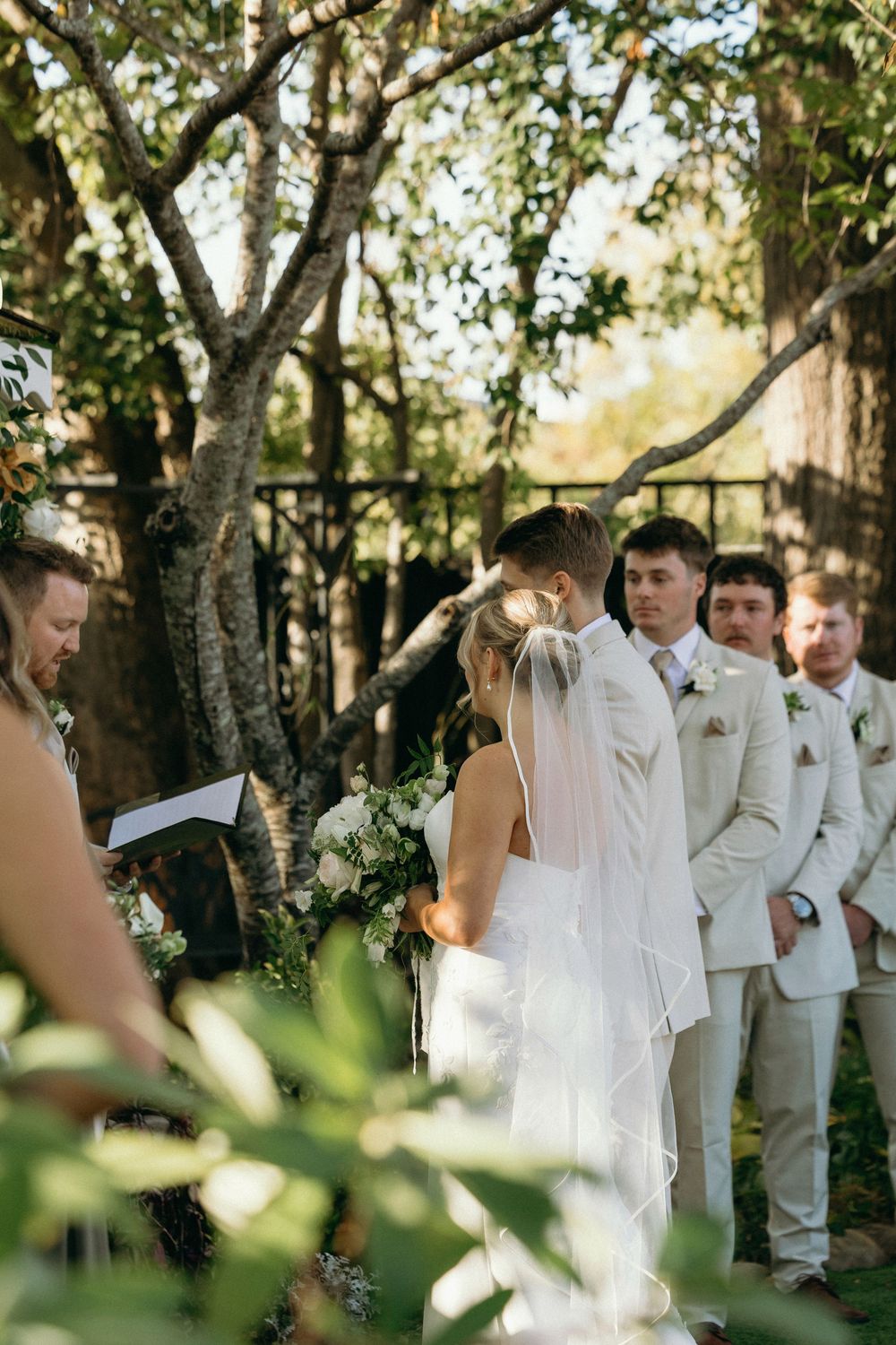 Wedding party gathered outdoors under trees in white attire during an intimate ceremony at Lillian Gardens in Newnan, Georgia