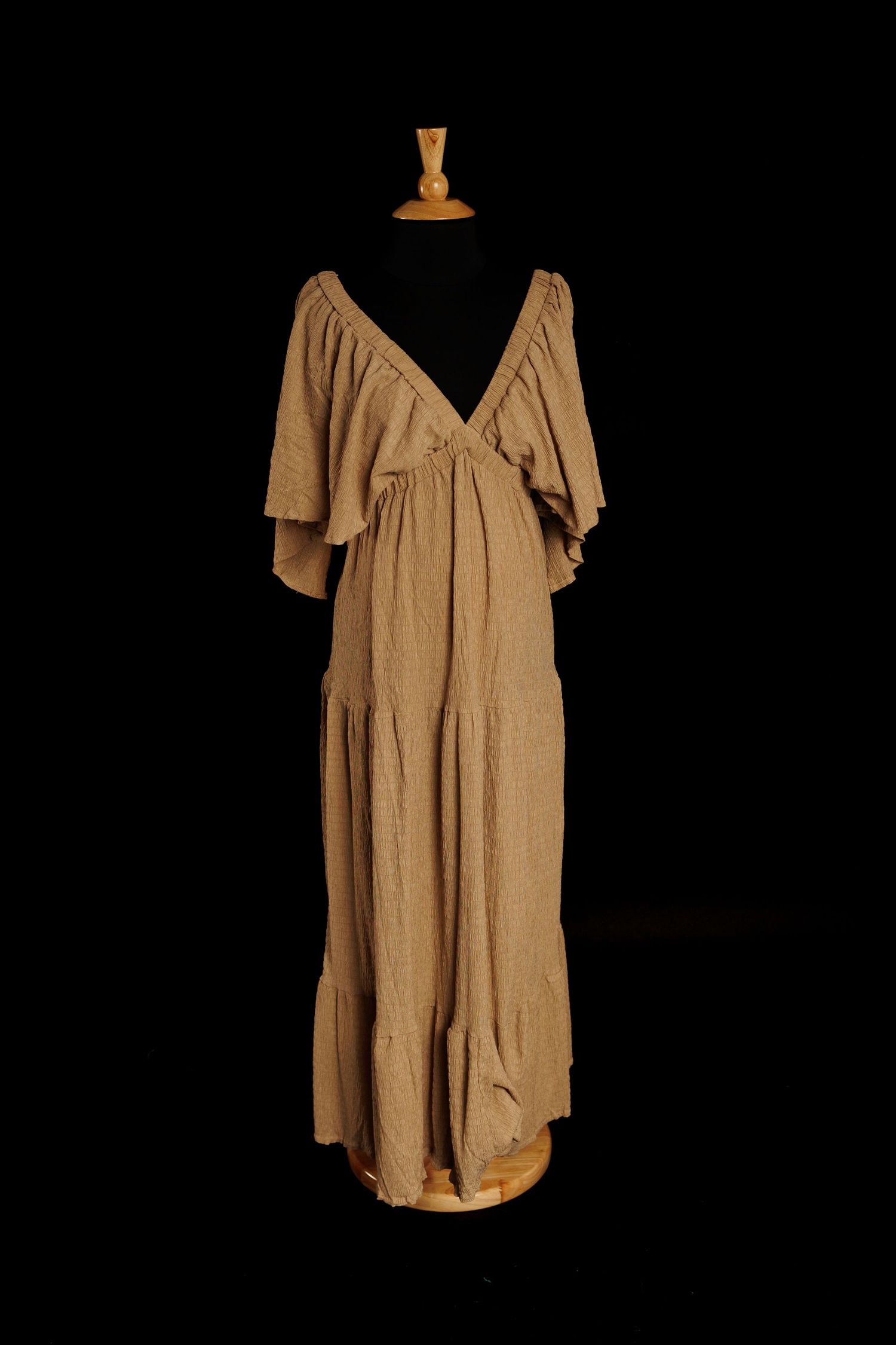 Light tan gauze maternity gown with wrap neckline, flutter sleeves, and tiered skirt on mannequin
