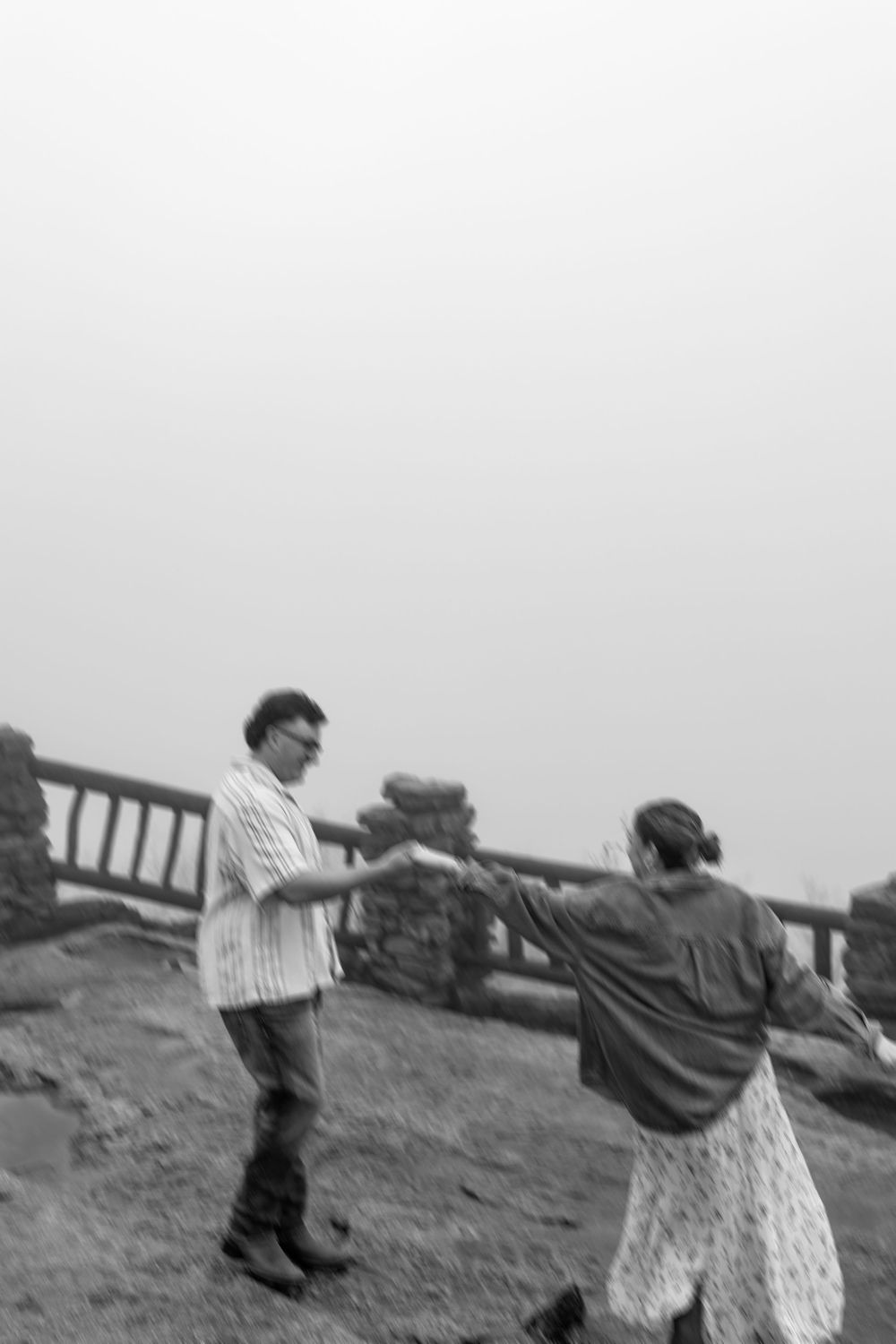 Blurred black and white photo of a couple dancing playfully on a foggy rocky overlook.