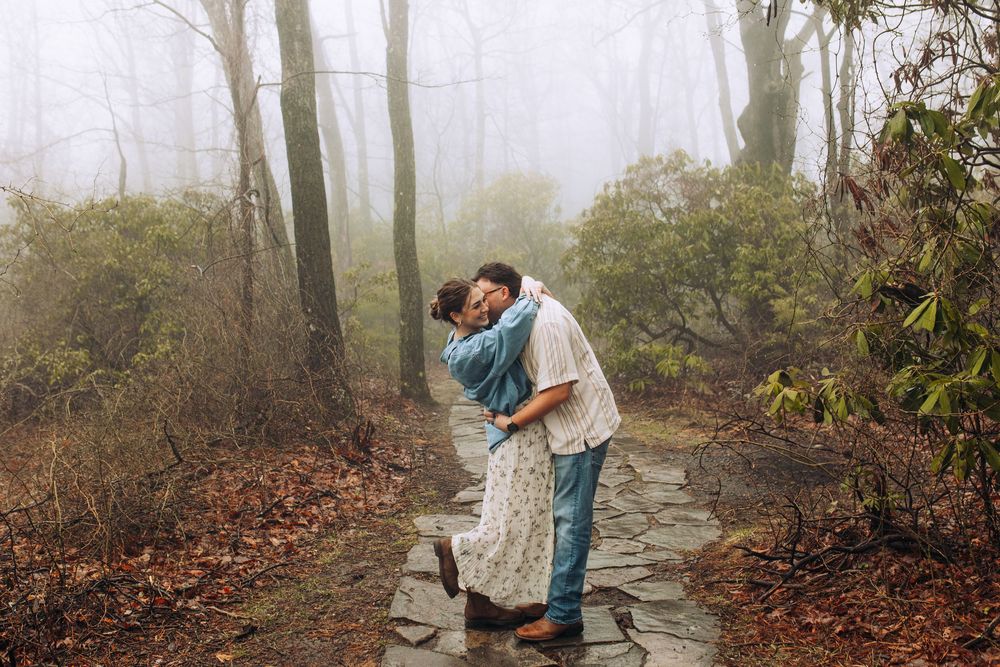 A couple sharing a passionate kiss on a stone forest path enveloped in atmospheric fog.