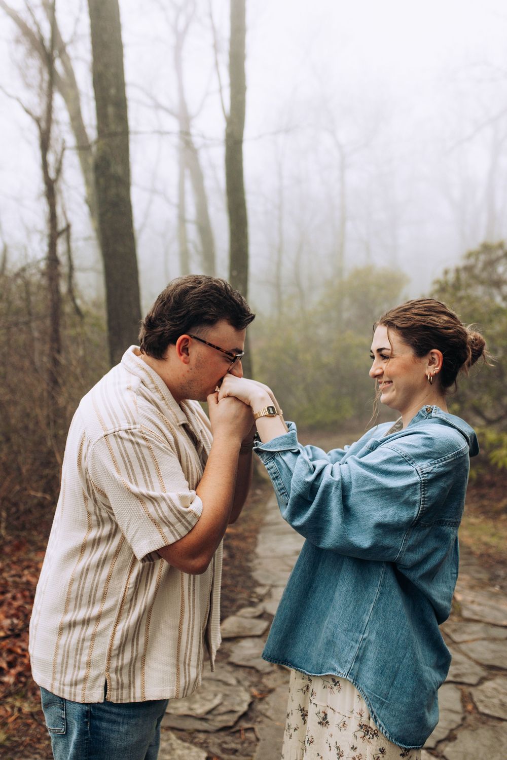 Couple sharing a romantic hand kiss moment on a foggy forest stone path.