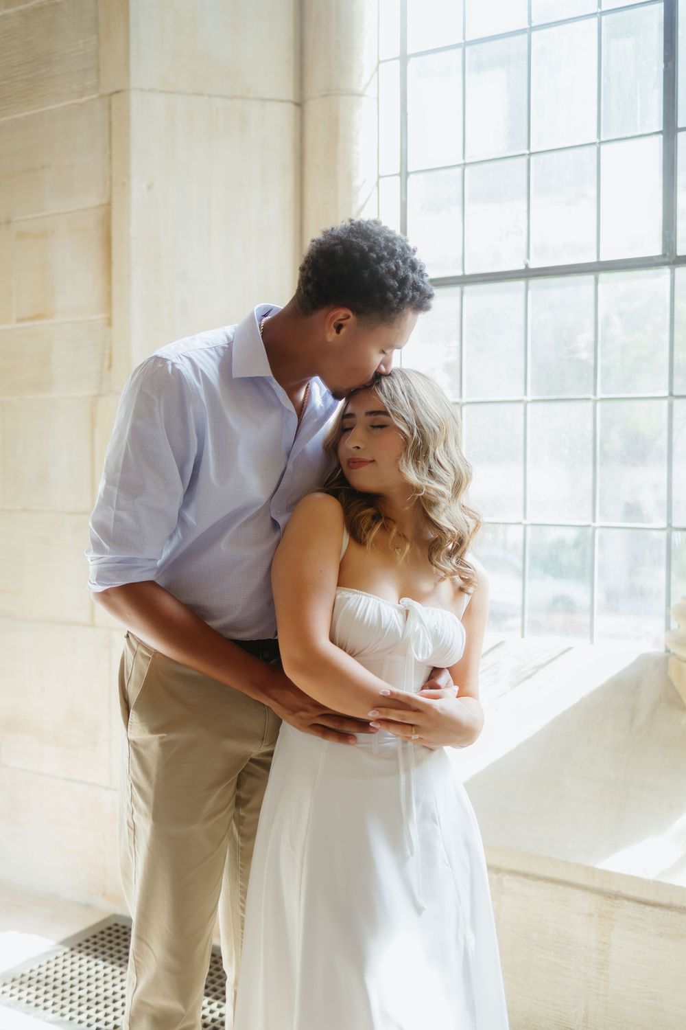 Romantic couple in white and khaki share intimate moments by a sunlit window in a minimalist setting.