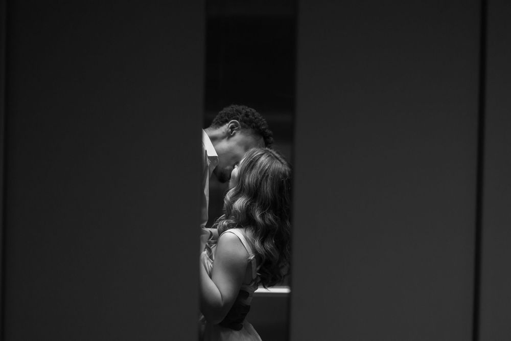 A romantic black and white photograph captured through a doorway shows a couple in an intimate embrace.