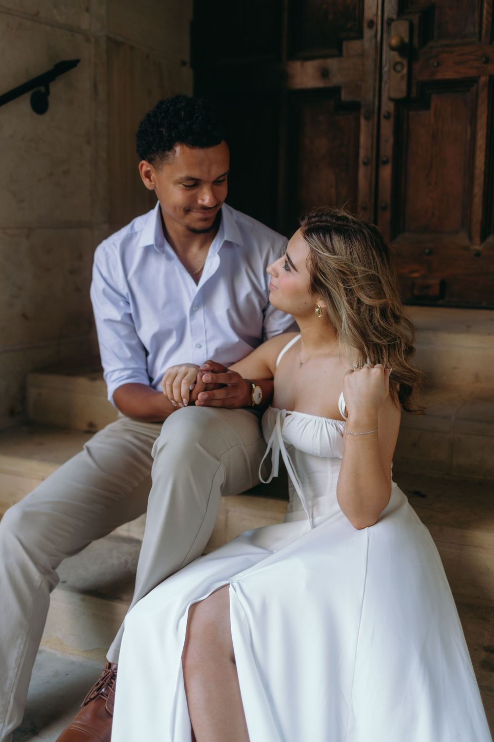 Couple in casual wedding attire shares intimate moments while seated in a rustic indoor setting.