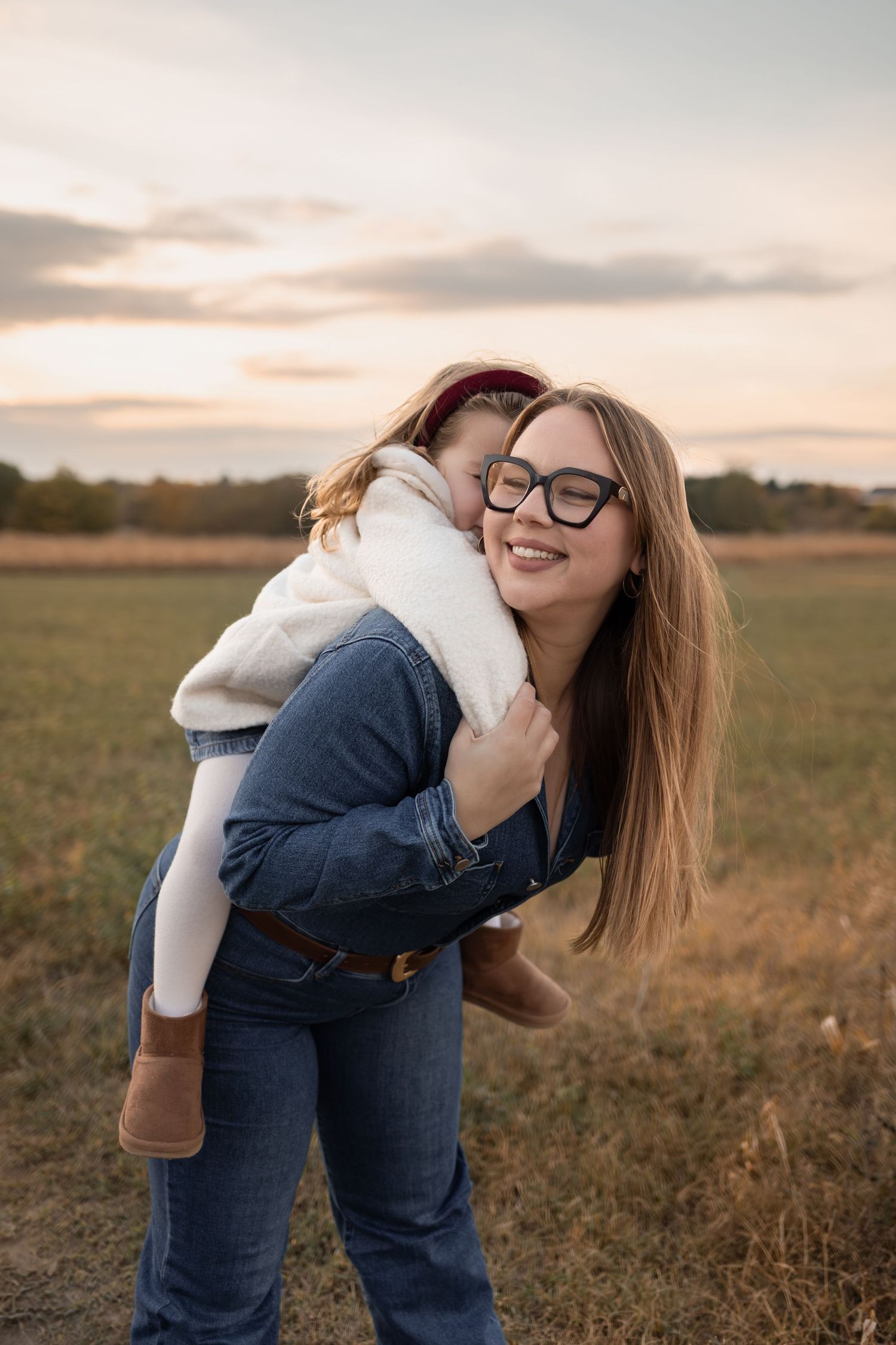Playful outdoor photoshoot in a field during sunset with casual denim and white outfit.