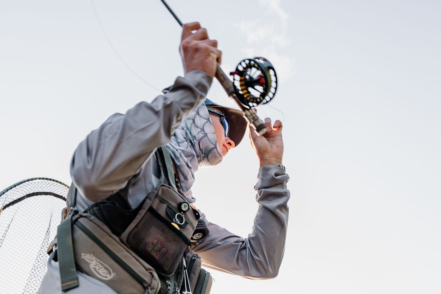 Person holding fly fishing reel against blue sky during outdoor fishing trip.