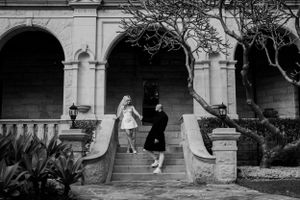 A couple in wedding attire walks up stone steps of an arched building.