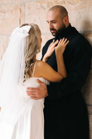 A couple embraces intimately against a stone wall during their wedding photoshoot.