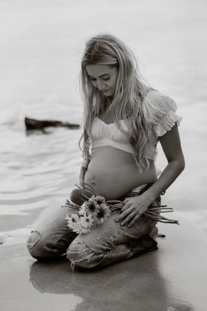 Black and white beach maternity portrait with seashell and flowing dress.