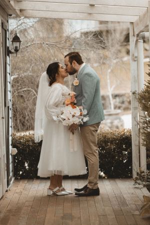 Intimate wedding moment captured under white pergola surrounded by natural foliage.