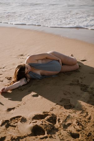 A person in a swimsuit lies peacefully on a sandy beach near ocean waves.