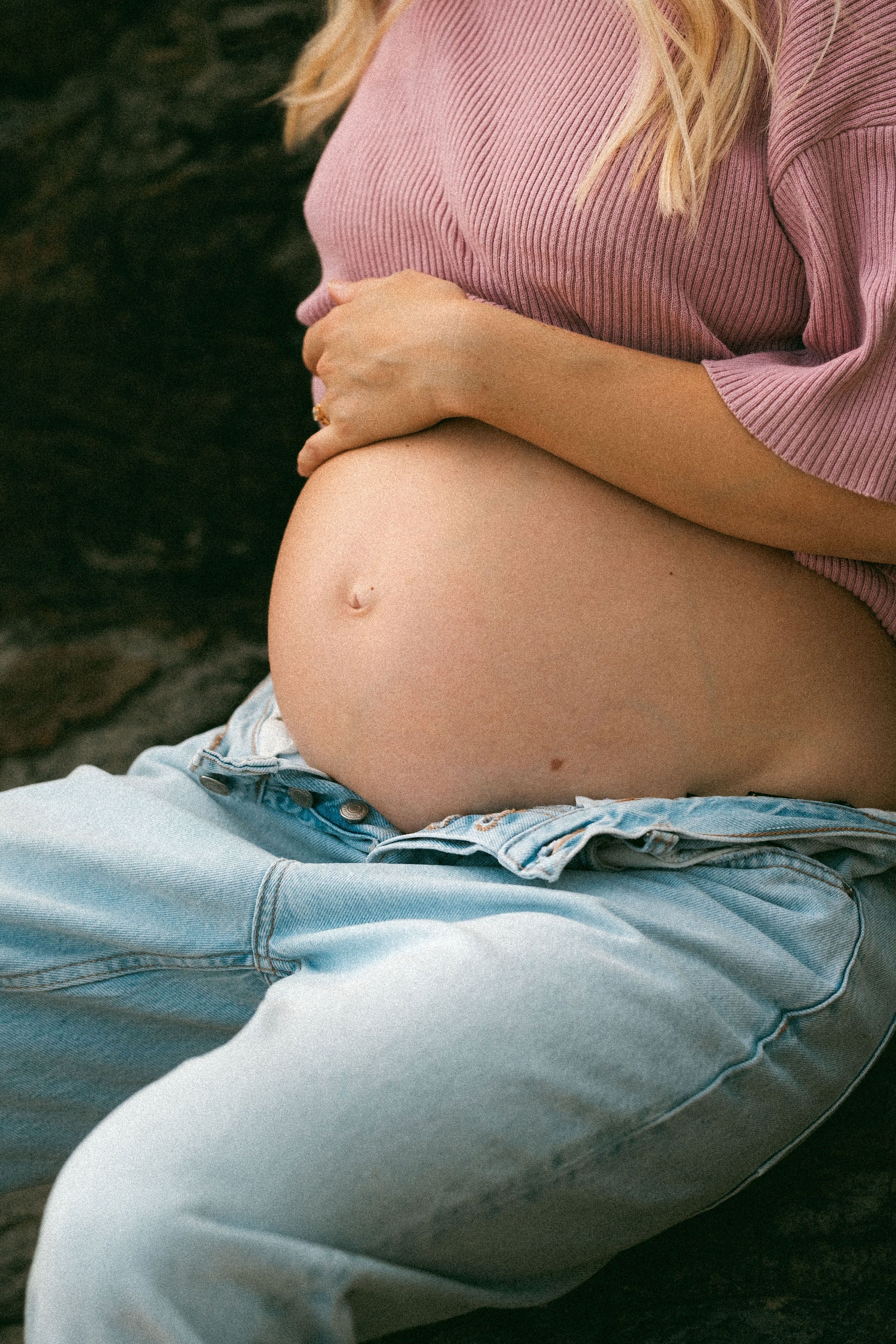 Sequential images showing a growing baby bump in light blue jeans and pink knit sweater over progressing pregnancy stages.