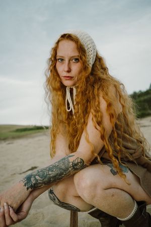 Portrait on beach wearing knit cap with rolling hills in background.