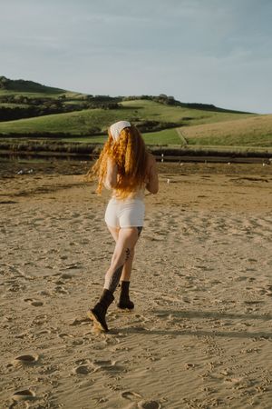 Figure with long hair running on beach with rolling hills in background.