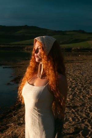 Sunset portrait on a beach wearing a white dress and crocheted hat.
