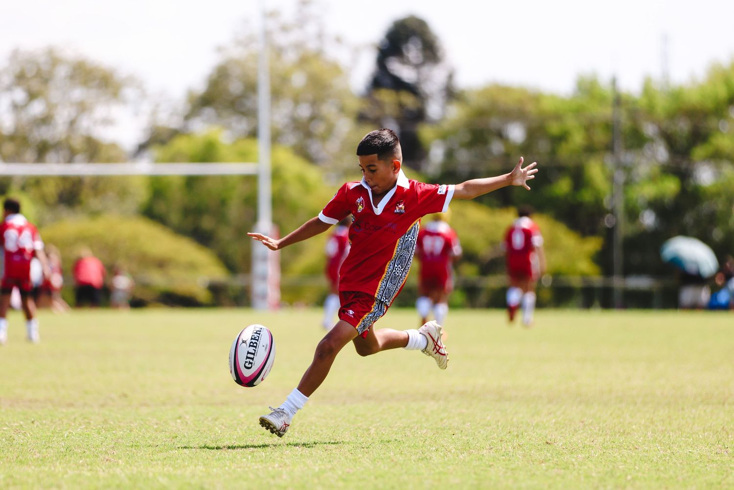 Rugby player kicking ball during match on sunny field.