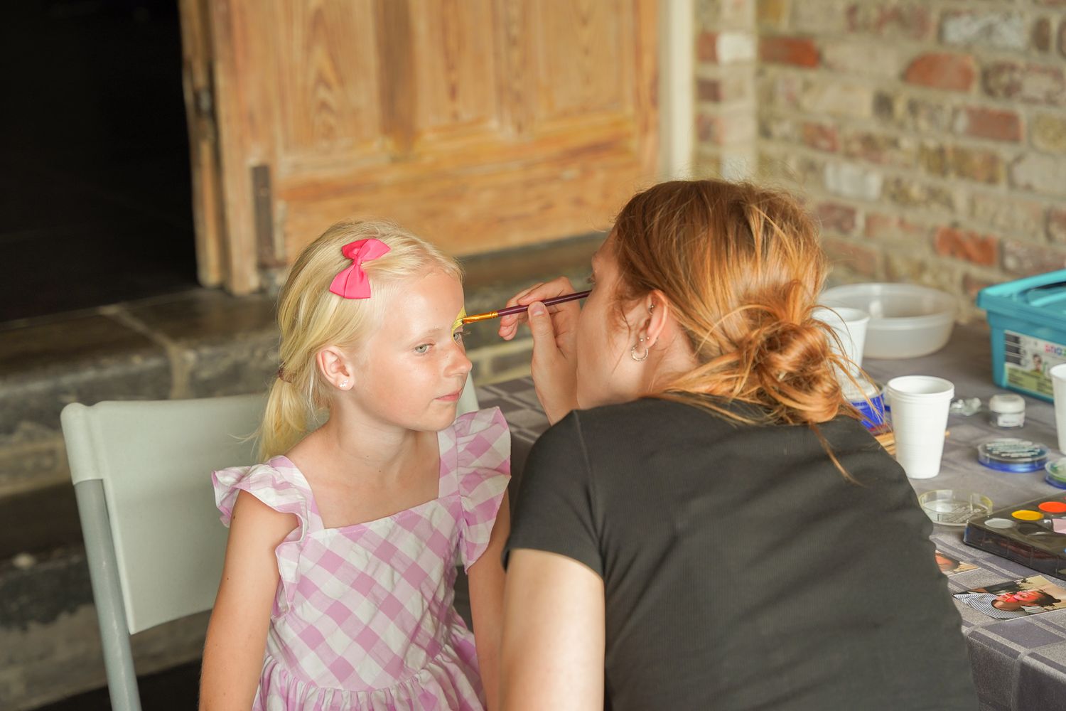 A face painting activity in progress at an indoor party setting with brick walls.