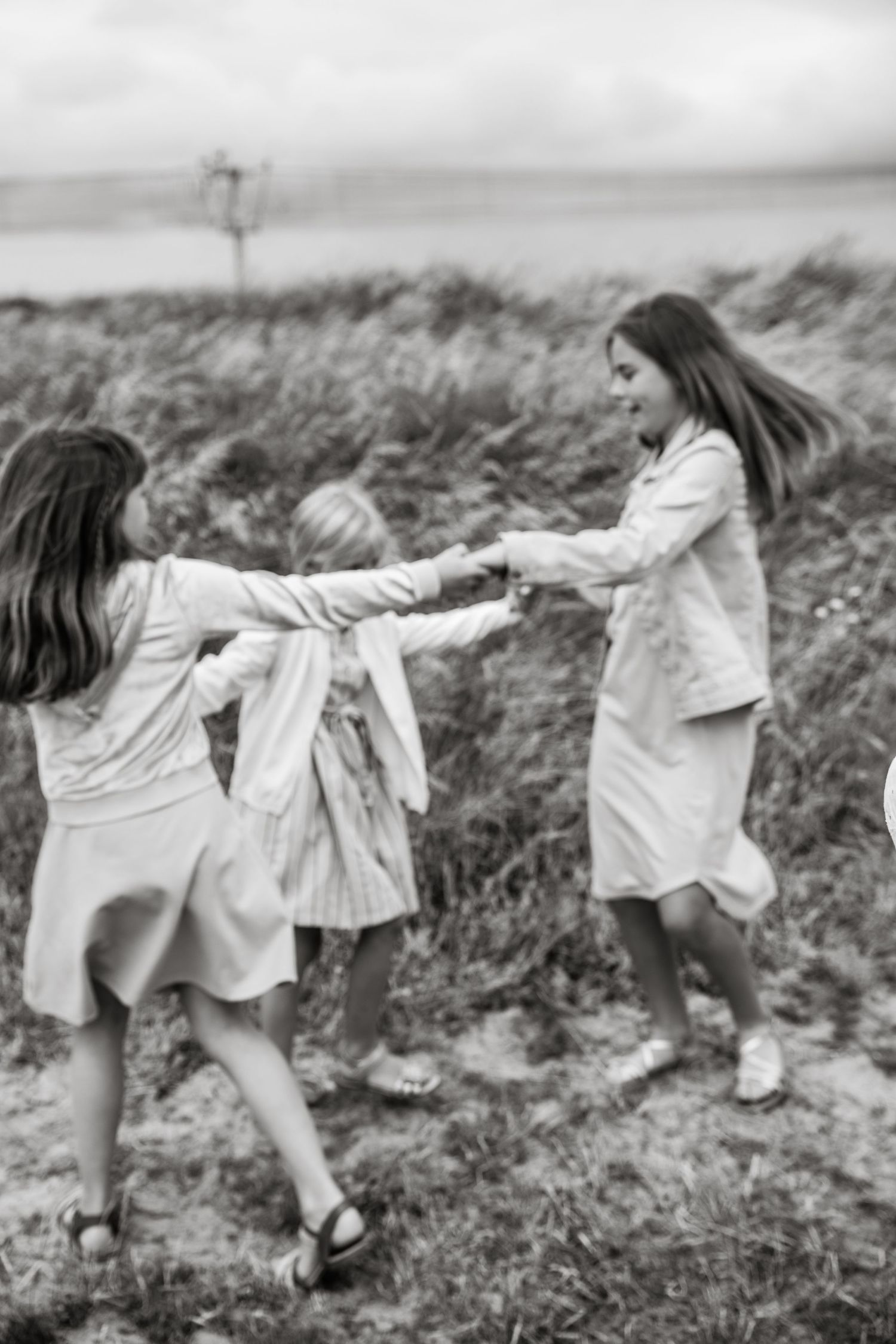 A black and white photo of people holding hands and spinning in a grassy field.